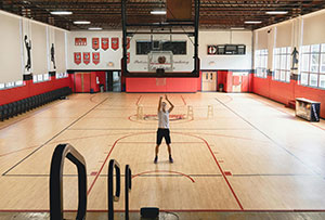 Basketball player shooting alone on an indoor basketball court inside a large school gymnasium.