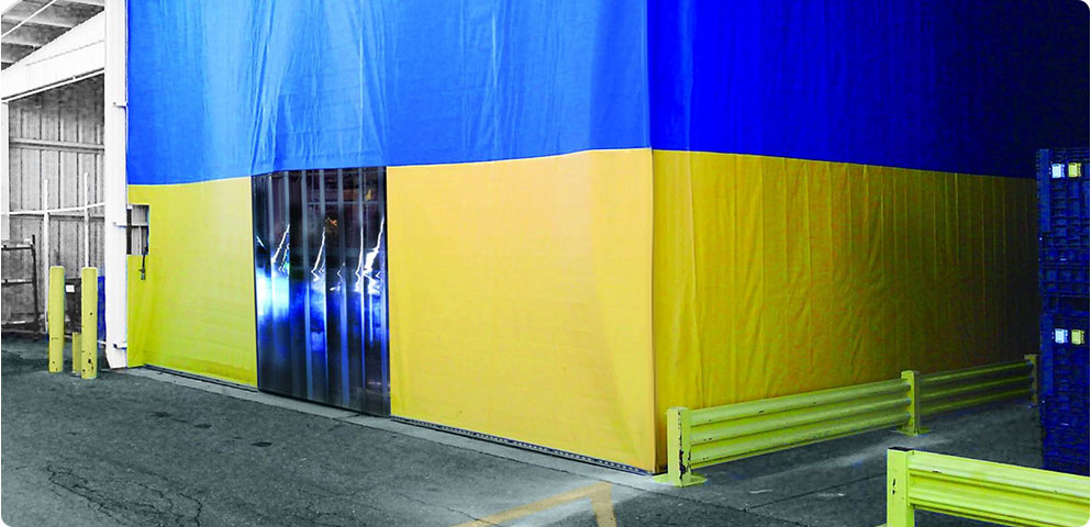 Heavy-duty blue and yellow industrial curtain with strip door entrance used to separate work areas and improve temperature control in a warehouse.